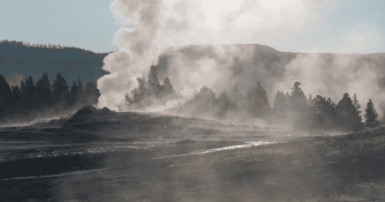 A Yellowstone Nemzeti Park Old Faithful gejzírje kitörés közben, ködös reggeli tájjal.